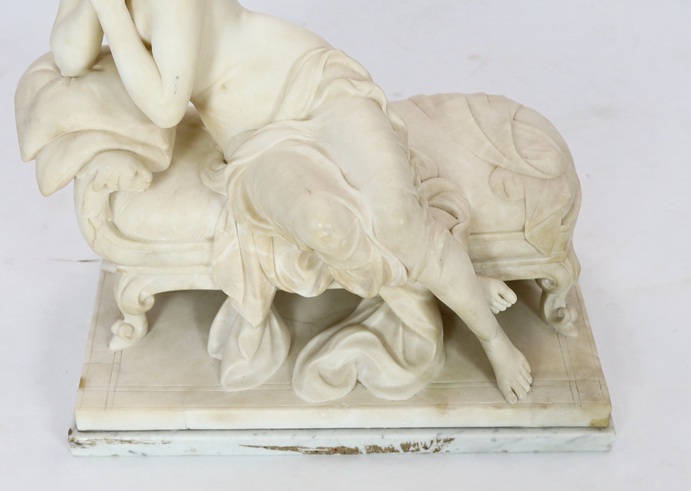 An early 20th century French carved white marble figure of a semi-clad woman seated upon a daybed, 50cm wide, 29cm deep, 52cm high